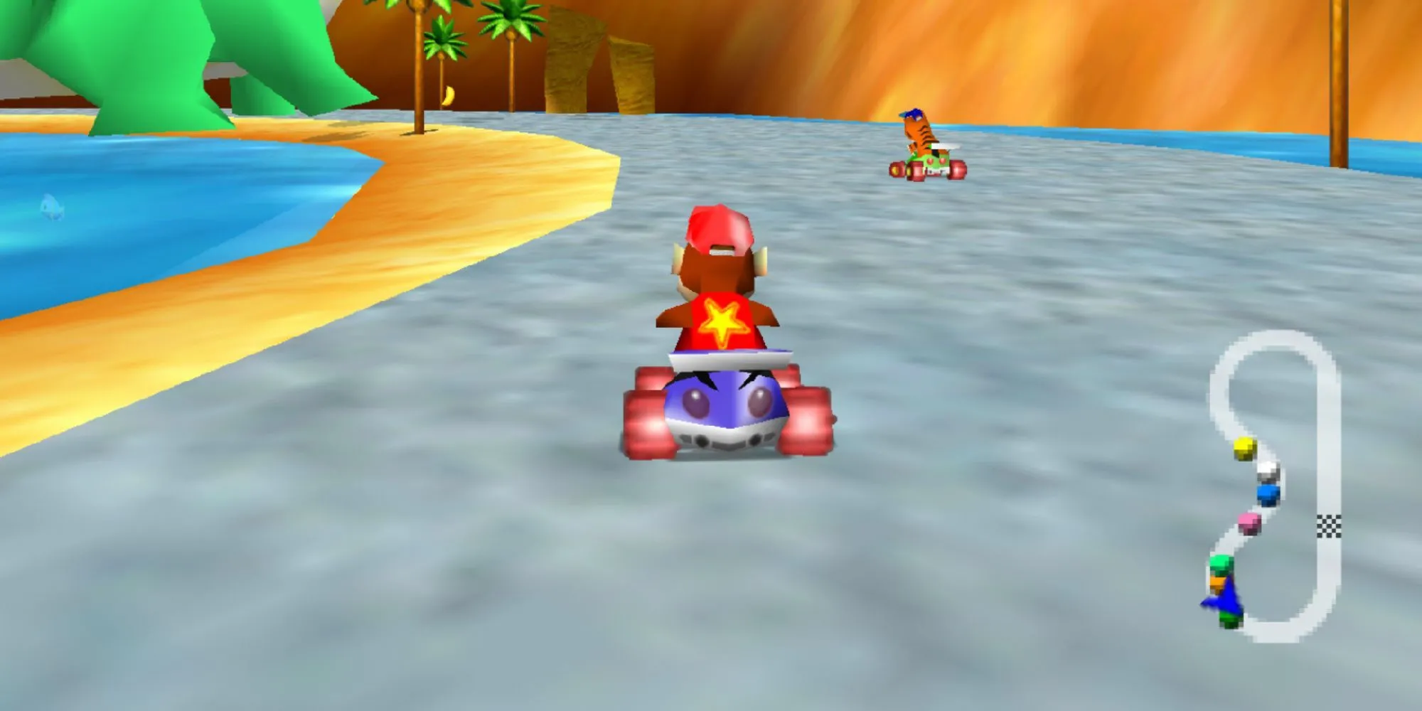 Diddy Kong Racing với Diddy Kong lái chiếc xe kart màu xanh dương, có ngôi sao sau lưng, đua cùng một chú hổ trên bãi biển đầy cát với nước ở hai bên